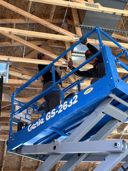 Two Five Star Mechanical techs hanging commercial ductwork from a Genie scissor lift