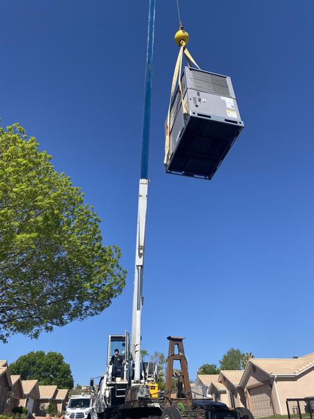 Crane lifting a new AC package unit to a residential rooftop