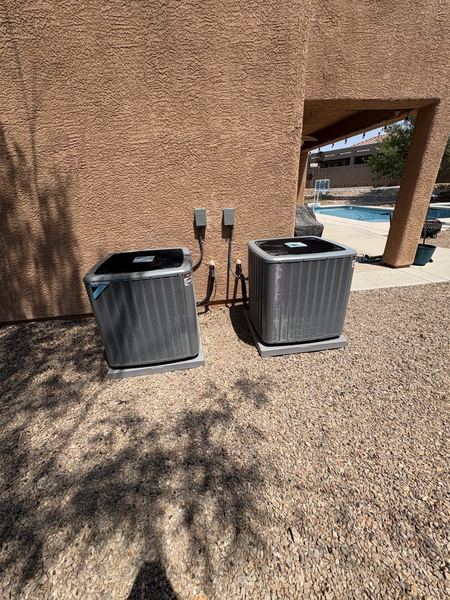 Two outdoor condensers installed side-by-side on a backyard pad